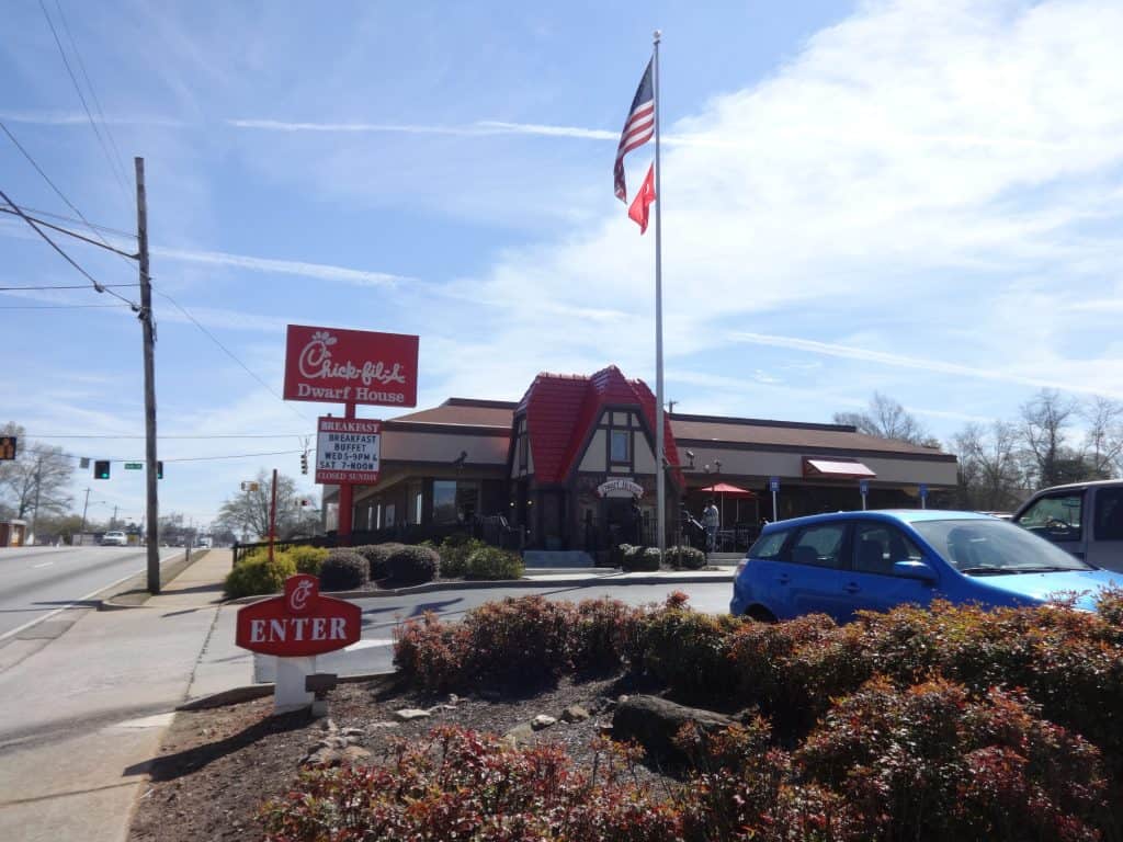 A Chick-fil-A restaurant with cars and a US flag outside