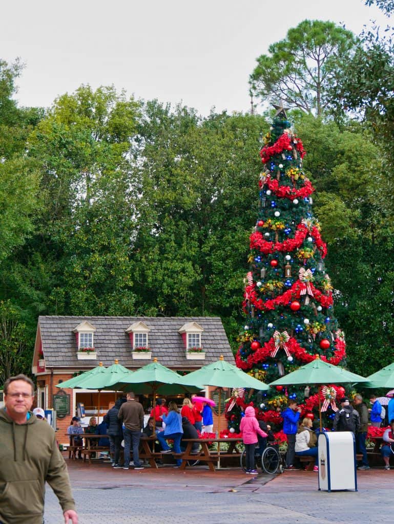 A Christmas tree with people eating underneath it under umbrellas at Epcot, Disney World at Christmas
