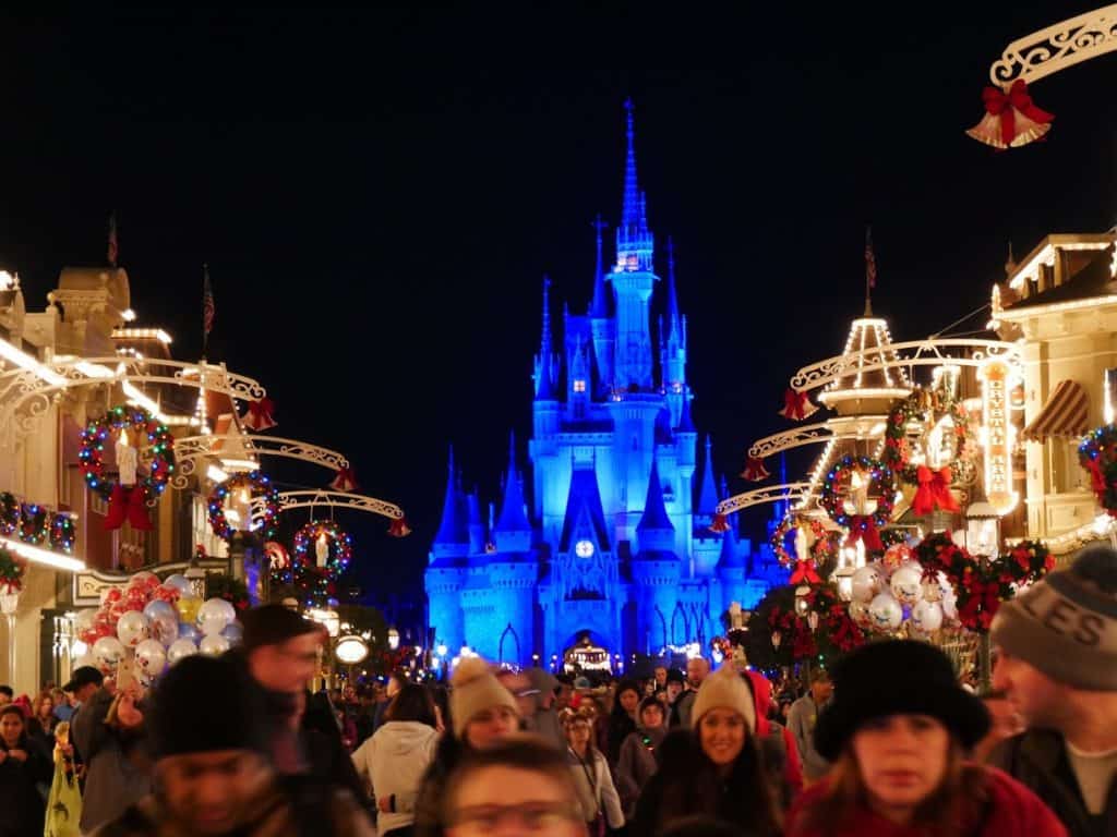 People walking down Main Street USA lit up at night at the Magic Kingdom in Disney World at Christmas