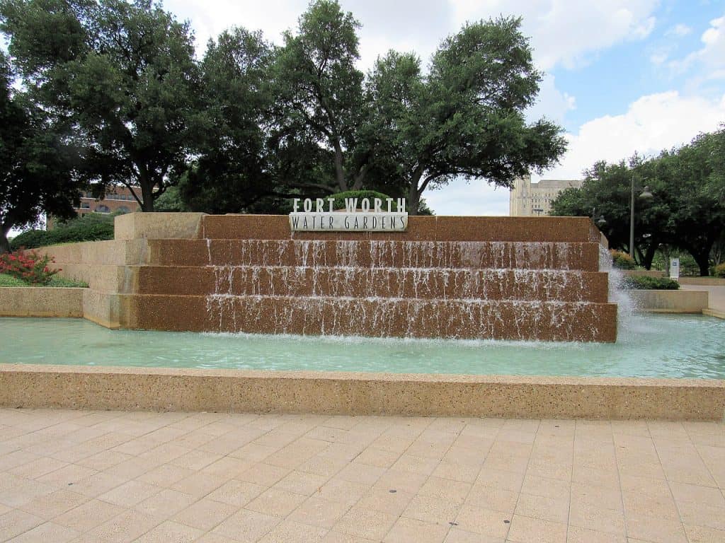 A pool of water and water flowing from a sign for the Fort Worth Water Gardens