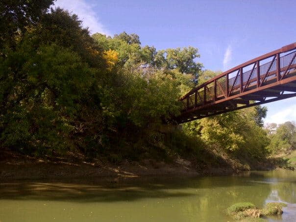 A river going past trees with a red bridge over it