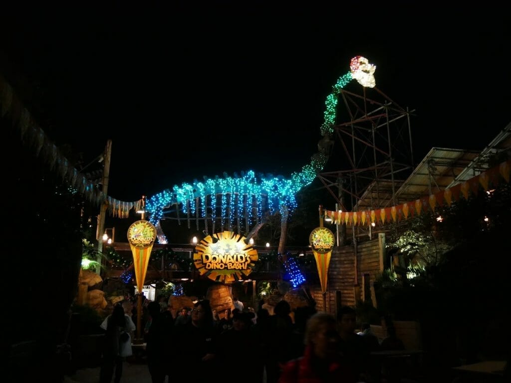 Large dinosaur with Santa hat and beard on lit up at night at Disney World's Animal Kingdom at Christmas