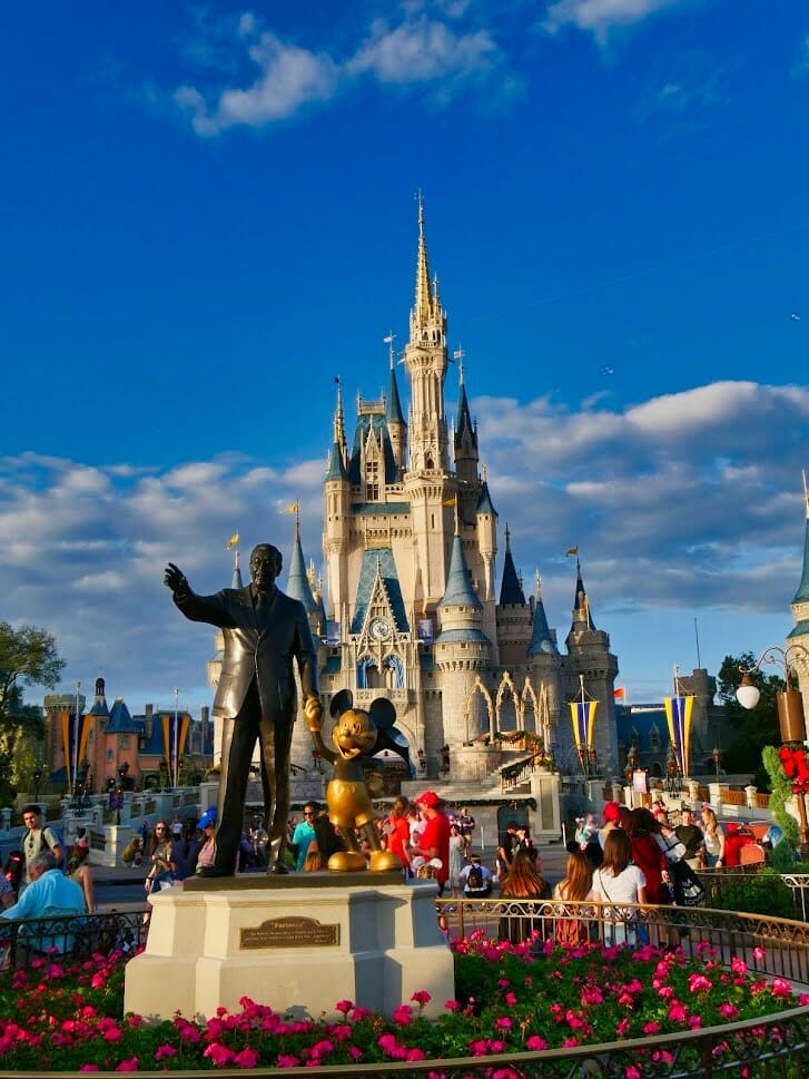 A Walt and Mickey Mouse statue in front of the Disney World Magic Kingdom castle