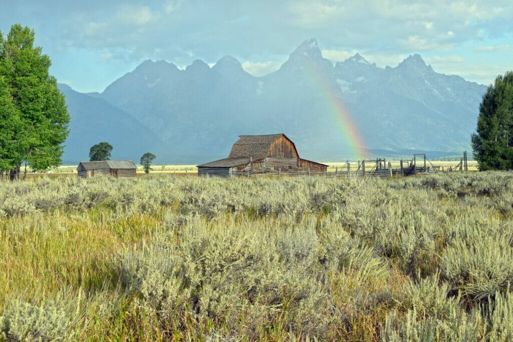 an old barn on a prairie with a rainbow and mountains in the background in Jackson Wyoming