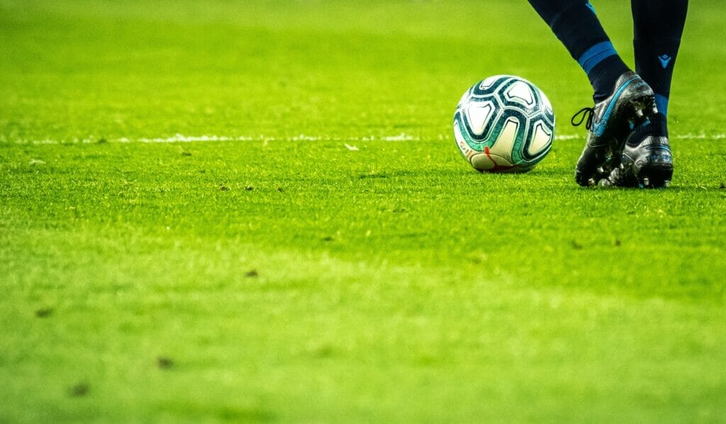 A soccer ball on a green field with a player's feet beside it