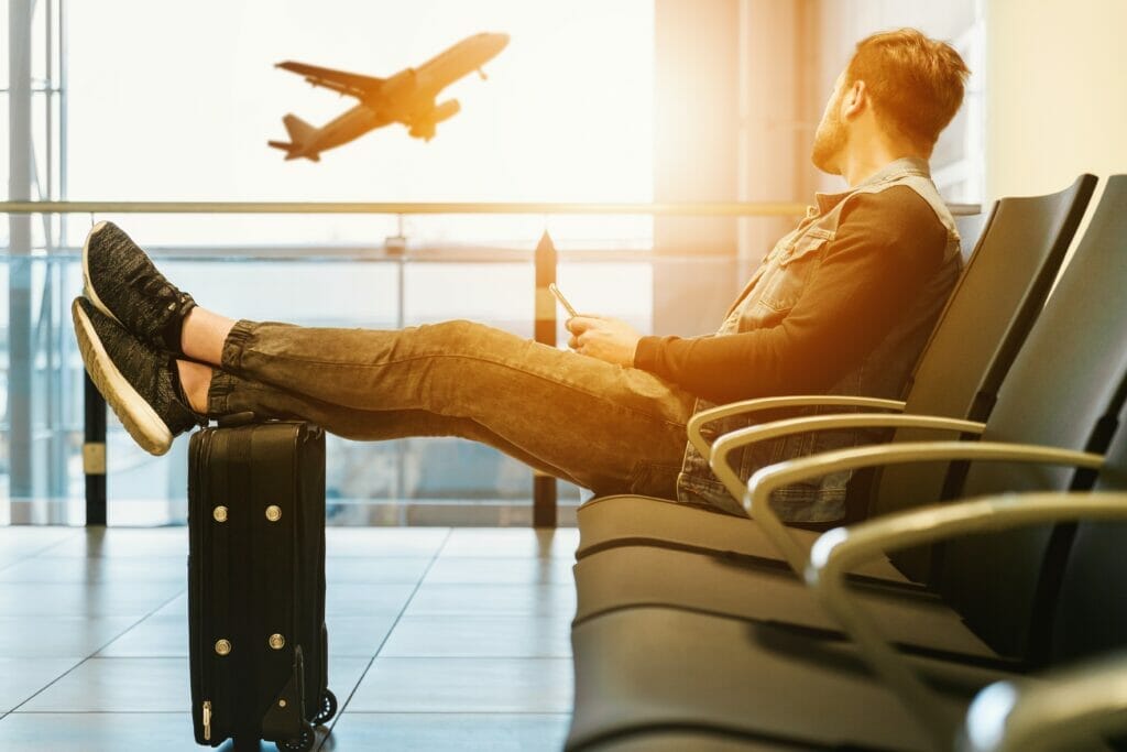A person sits in a chair at an airport and watches a plane take off out the window