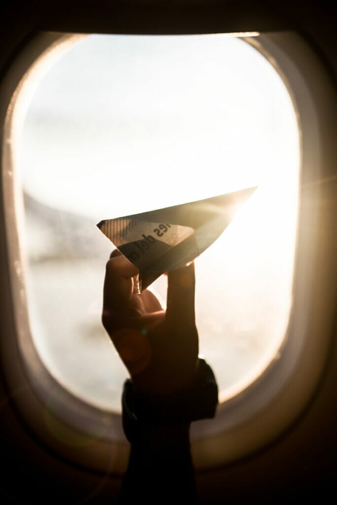 A paper plane held up in front of an airplane window