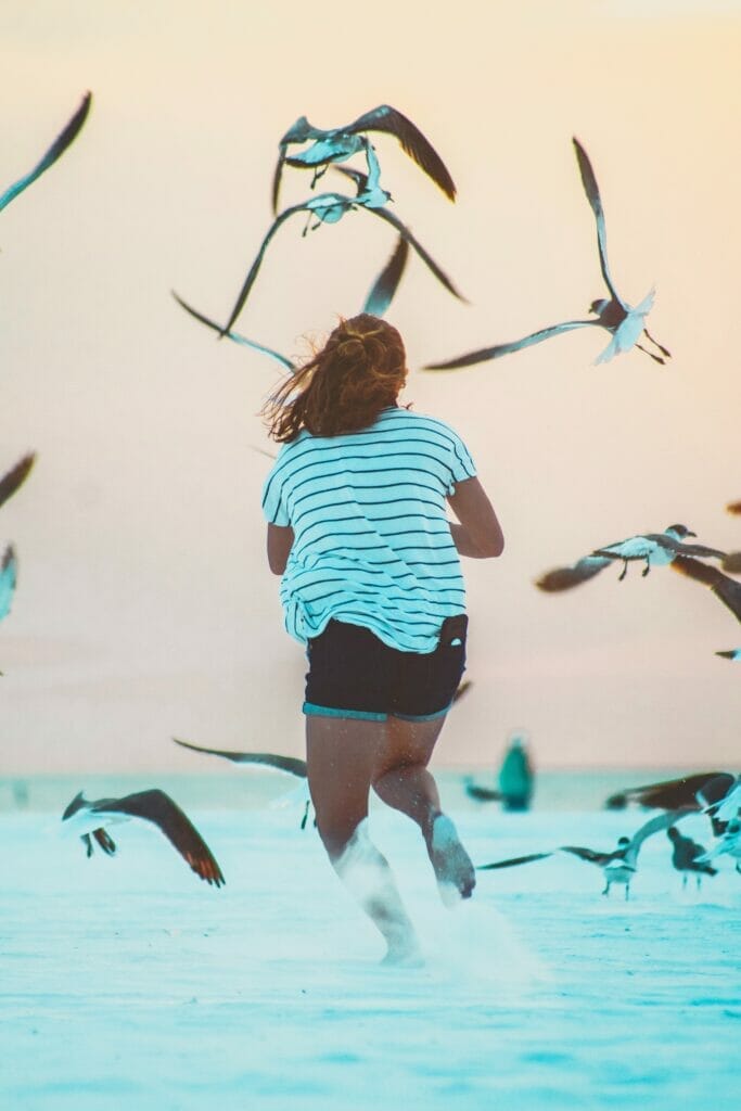 girl running through sand with birds flying
