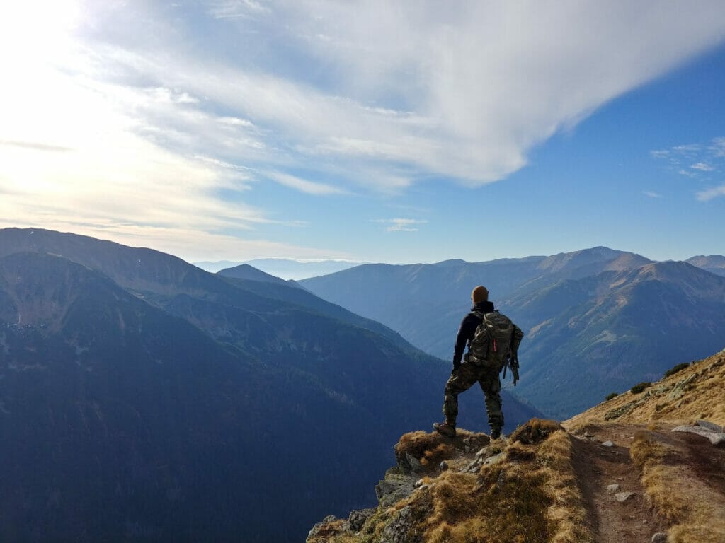 person standing on edge of cliff looking at mountains