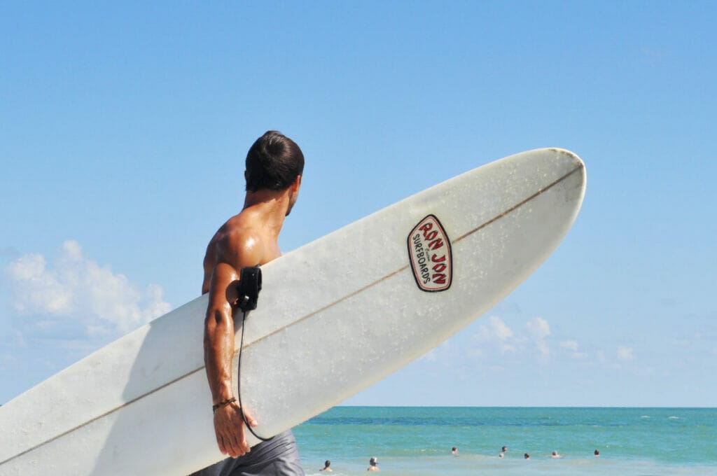 man holding ron jon surfboard at the beach