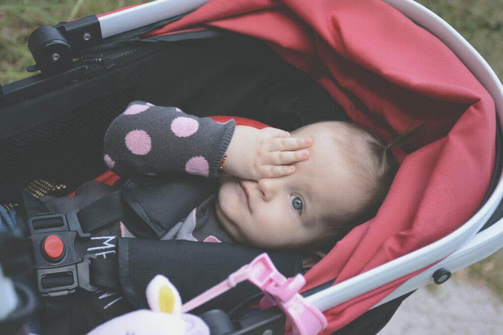 baby lying in stroller with one eye covered