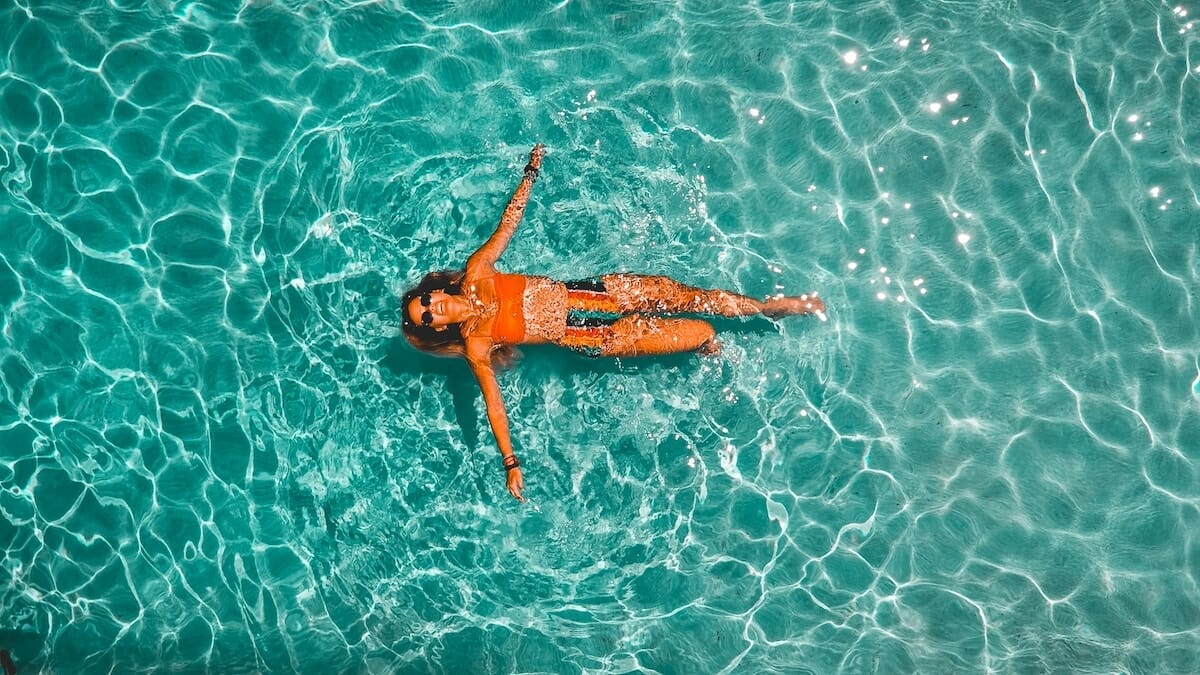 A woman smiling and floating on her back in a pool of clear blue water