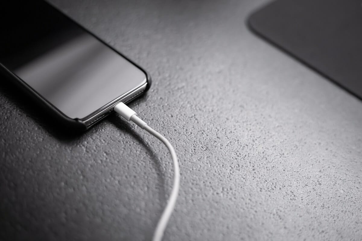 A smartphone plugged into a white USB charging cord