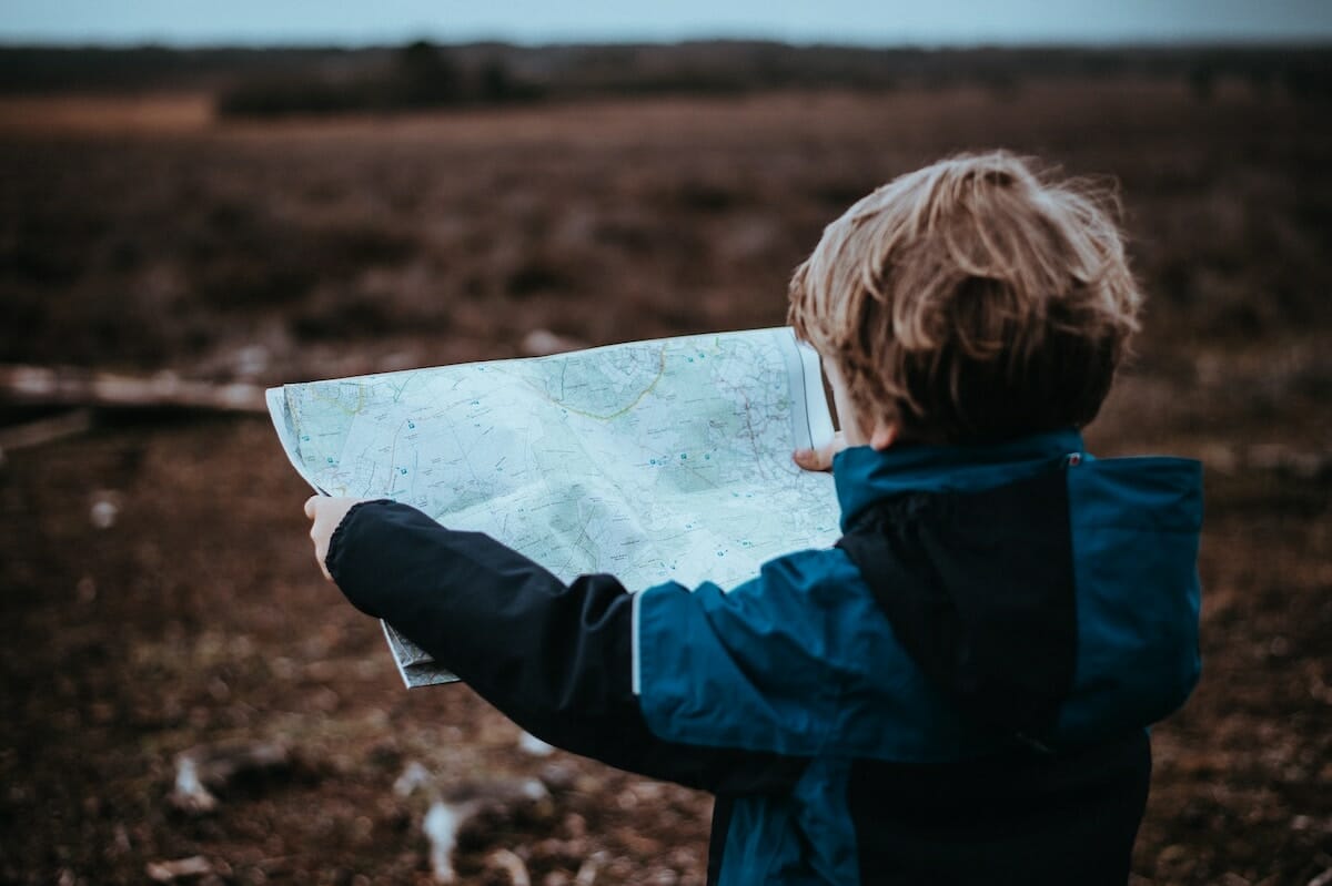 A young child is seen from behind, holding a paper map with both hands and looking at it