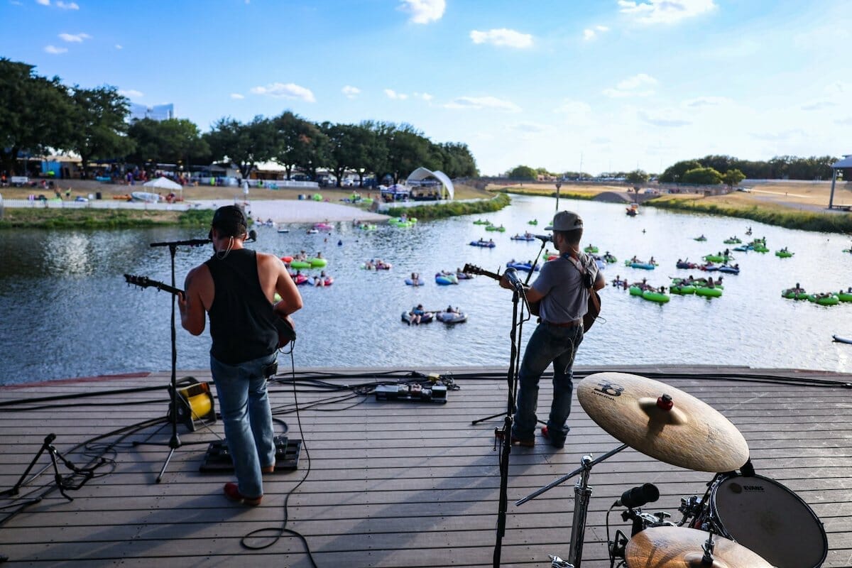 Performers on a stage look out over a crowd in tubes on Trinity River during Fort Worth's Rockin the River event