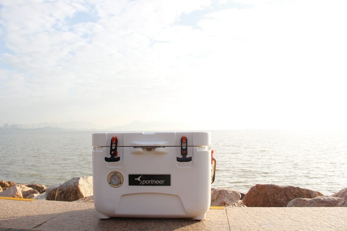 A white cooler rests on concrete near the seaside on a sunny day