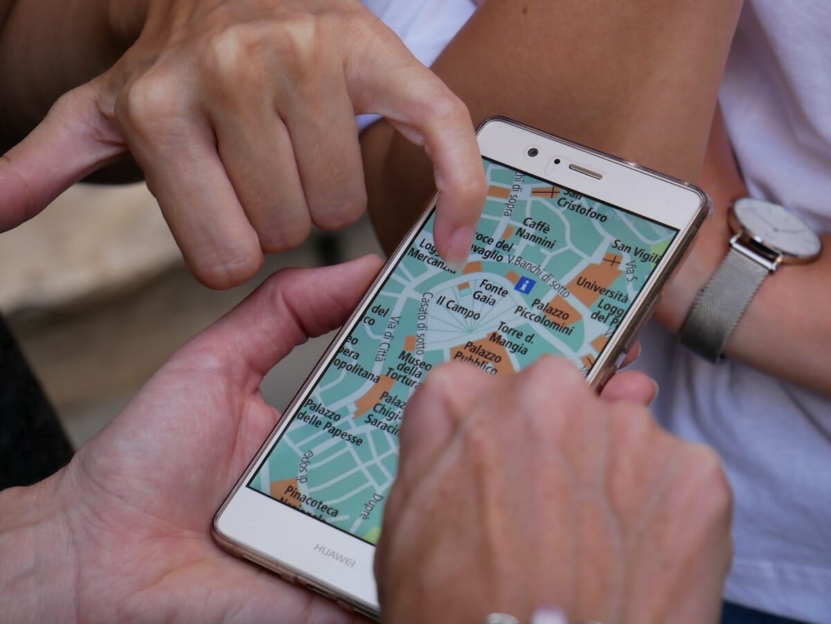 Close up of a group of different people's hands surrounding and pointing at a phone with a maps app open