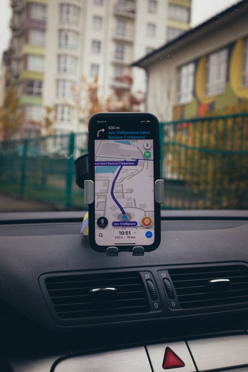 A smartphone with the GPS app open, held in a phone holder that is attached to the dashboard of the car