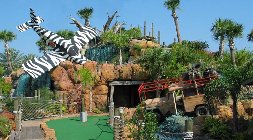 Congo River Golf course in Orlando, featuring scenes of a crashed plane over a waterfall, a jeep full of safari gear, and the green golf course leading toward a cave.
