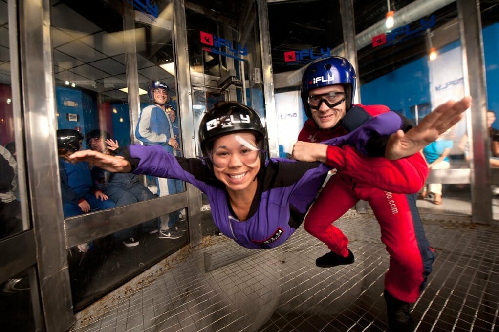 an indoor skydiver at iFly Orlando smiles at the camera with their instructor at their side