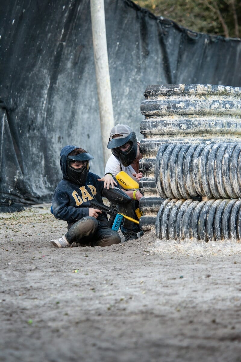 An adult and a child hide behind a barricade while playing paintball in Orlando Florida