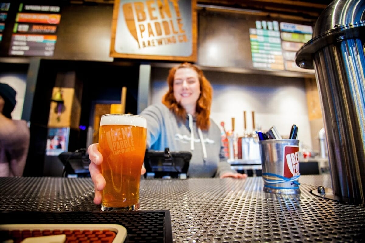 a smiling bartender reaches across the bar with a glass of beer in hand at Bent Paddle Brewing Company in Duluth, MN