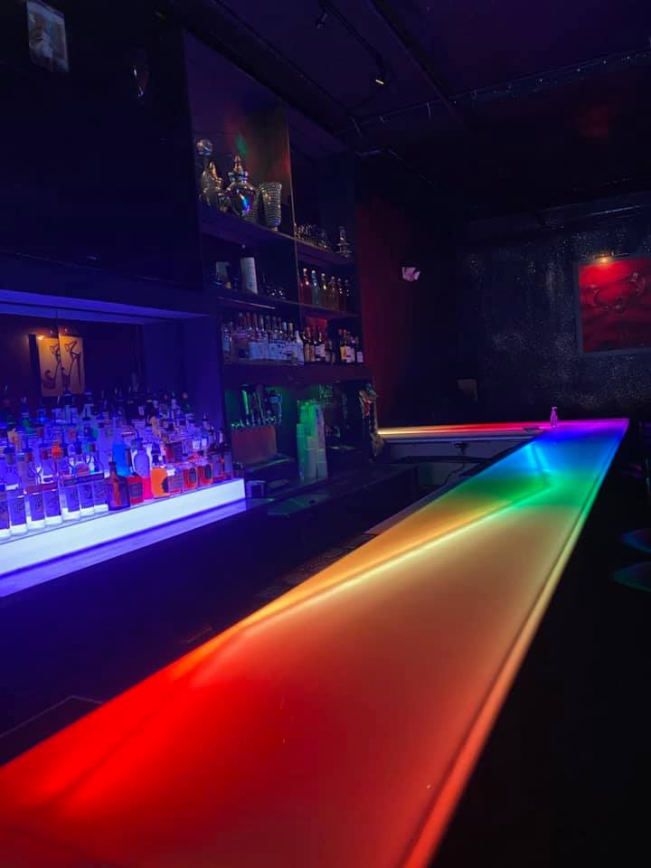 view of the bar which is lit up in rainbow lights at Duluth Flame nightclub