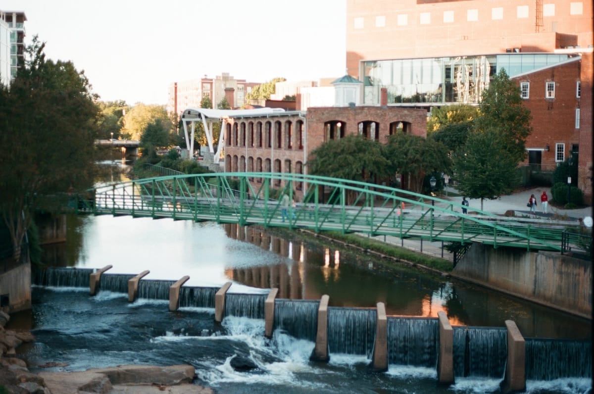 more waterfalls in downtown Greenville, South Carolina, under a green pedestrian bridge