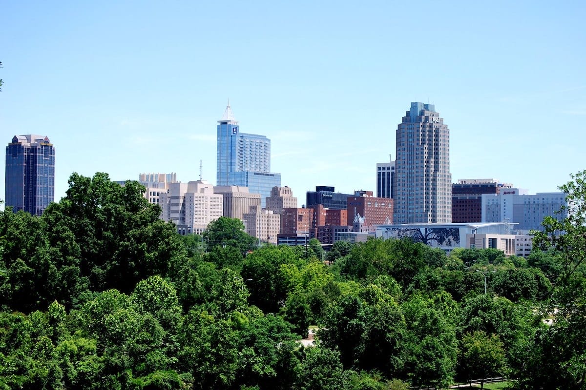 downtown Raleigh skyline behind a forest of green trees