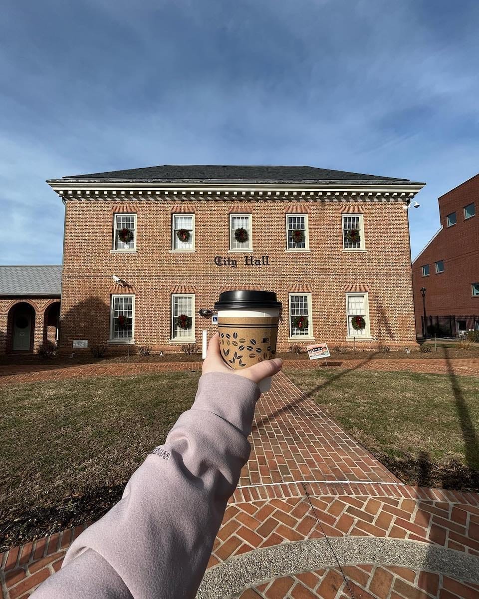 a to-go coffee cup held in front of the Dover City Hall 