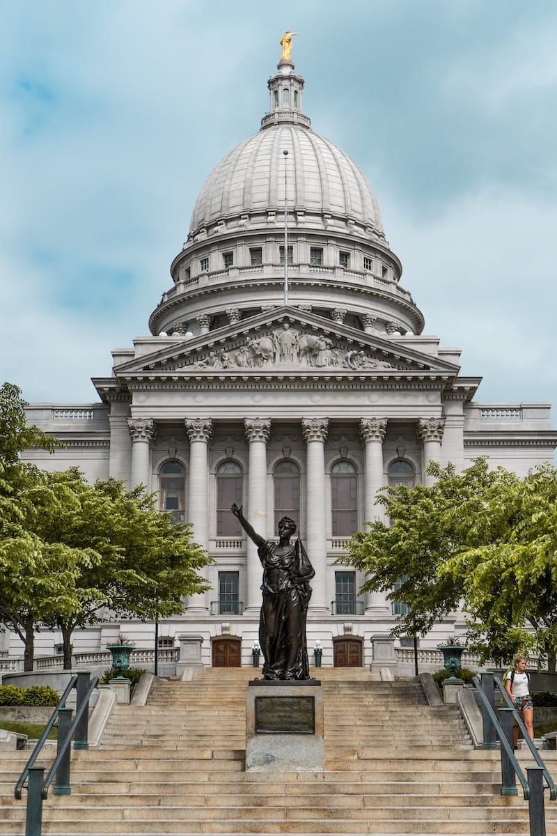 capitol building in Madison Wisconsin, featuring a bronce sculpture in front and a dome on top likening to the US capitol in DC